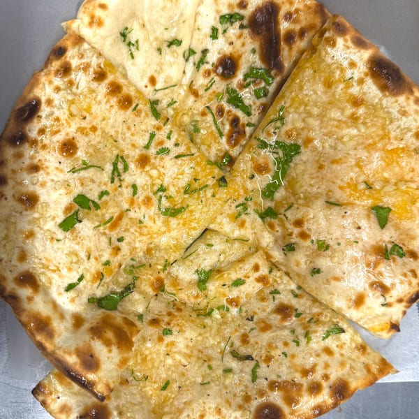 Close-up of golden-brown garlic naan bread, cut into triangles and topped with fresh green herbs.
