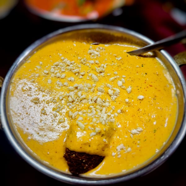 Close-up of Sherpa Grill 2's Indian Nepali curry, a rich yellow dish topped with nuts in a metal bowl.