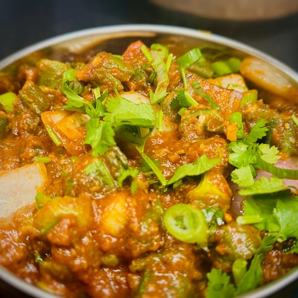 Close-up of a vibrant Indian dish with okra, onions, and cilantro in a rich orange sauce.