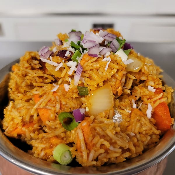 Close-up of Indian Nepali biryani with rice, vegetables, red onions, and green onions in a metal bowl.