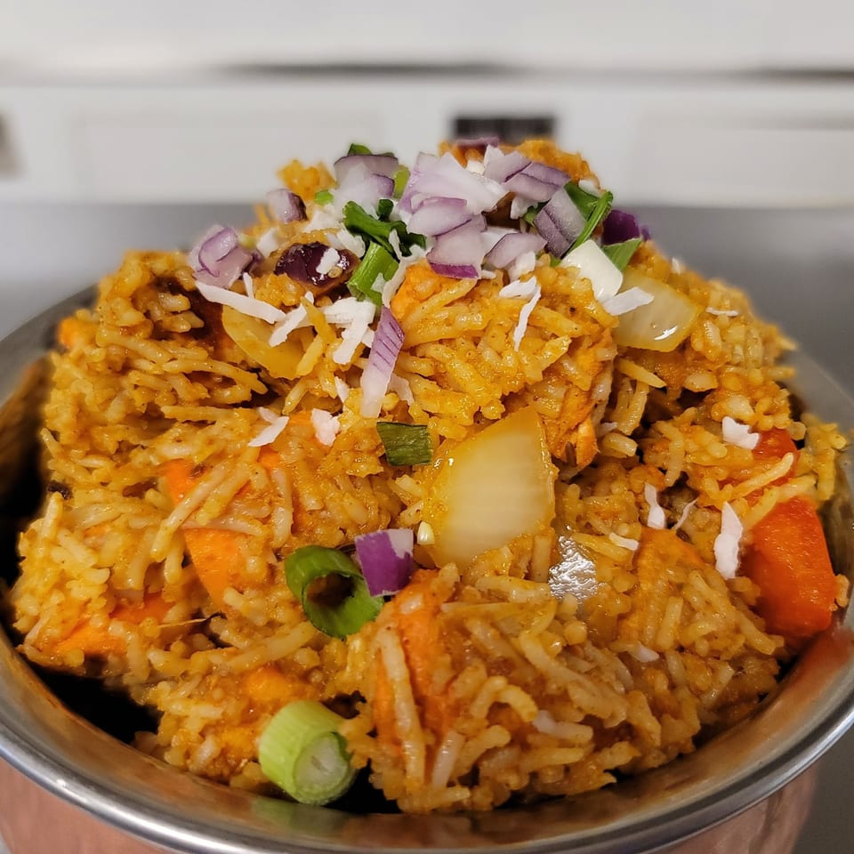 Close-up of Indian Nepali biryani with rice, vegetables, red onions, and green onions in a metal bowl.