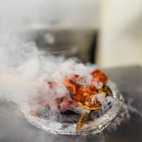 Sizzling Indian Nepali dish with red sauce and vegetables, emitting dramatic white smoke from a foil-lined plate.