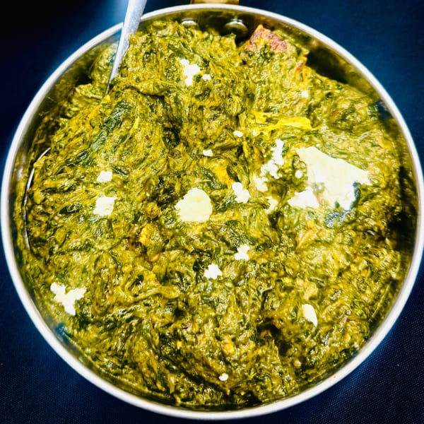 Close-up of vibrant green Palak Paneer, an Indian spinach and cheese dish, in a metal bowl.