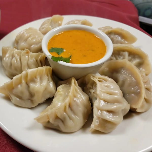 A plate of Sherpa Grill 2 Indian Nepali Restaurant momos with a side of orange dipping sauce.